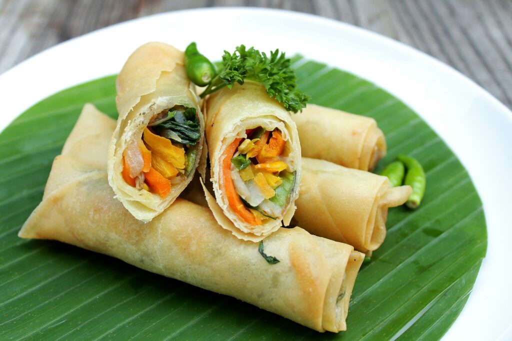 Fresh homemade crispy vegetable spring rolls served with sweet chili dipping sauce on a black plate, showcasing a crunchy golden wrapper and colorful Asian-style filling