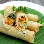 Fresh homemade crispy vegetable spring rolls served with sweet chili dipping sauce on a black plate, showcasing a crunchy golden wrapper and colorful Asian-style filling