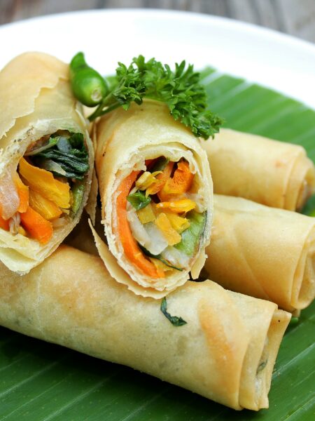 Fresh homemade crispy vegetable spring rolls served with sweet chili dipping sauce on a black plate, showcasing a crunchy golden wrapper and colorful Asian-style filling