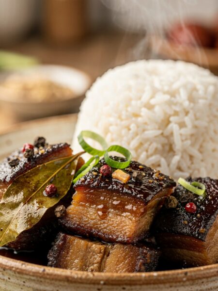 A bowl of authentic Filipino pork adobo with tender pork belly chunks in a glossy garlic soy sauce, served over a bed of steaming white rice